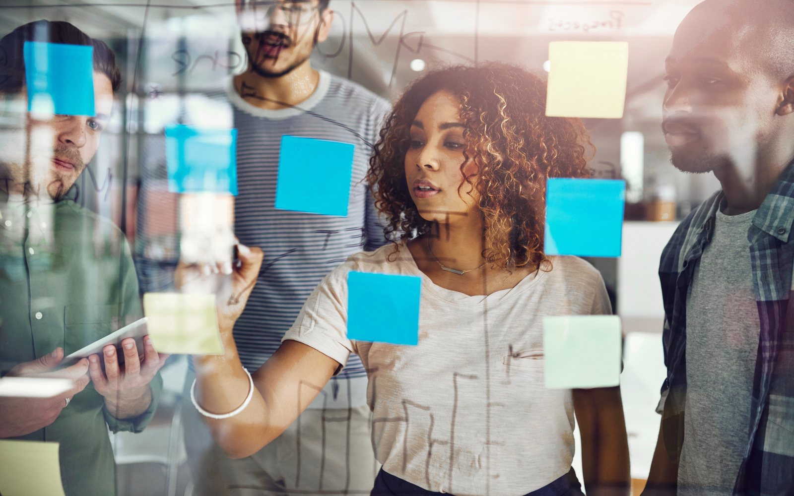 Colleagues working through a problem together with sticky notes on a glass wall